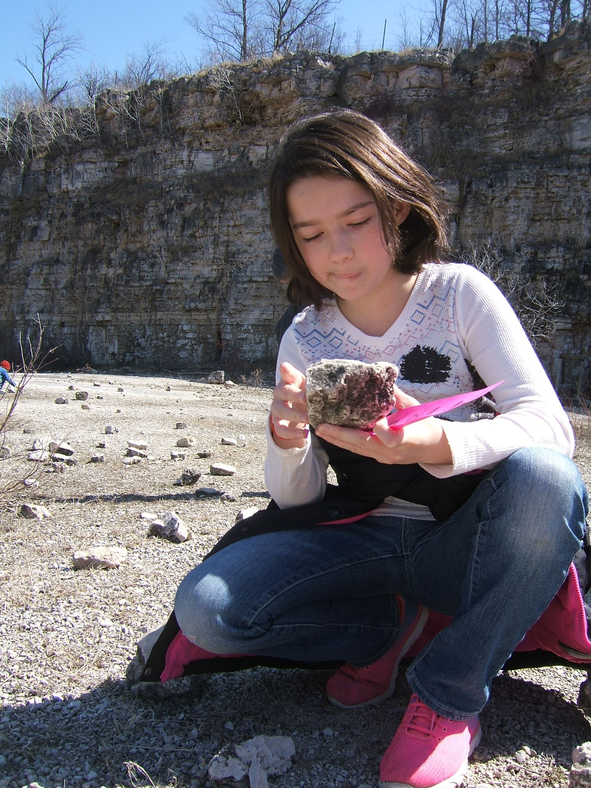 girl looking at a rock with a fossil in it