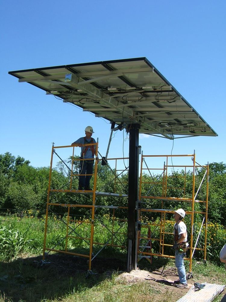 Two men standing under a solar panel looking up. One man is on the ground and the other is on yellow
